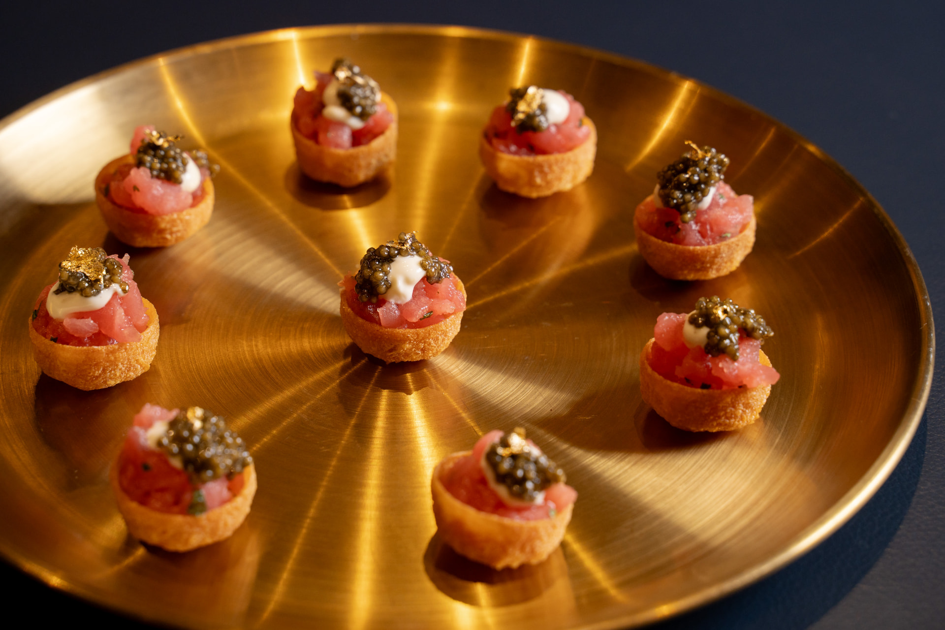 Tuna tartare canapés with caviar and gold leaf presented on a brass tray