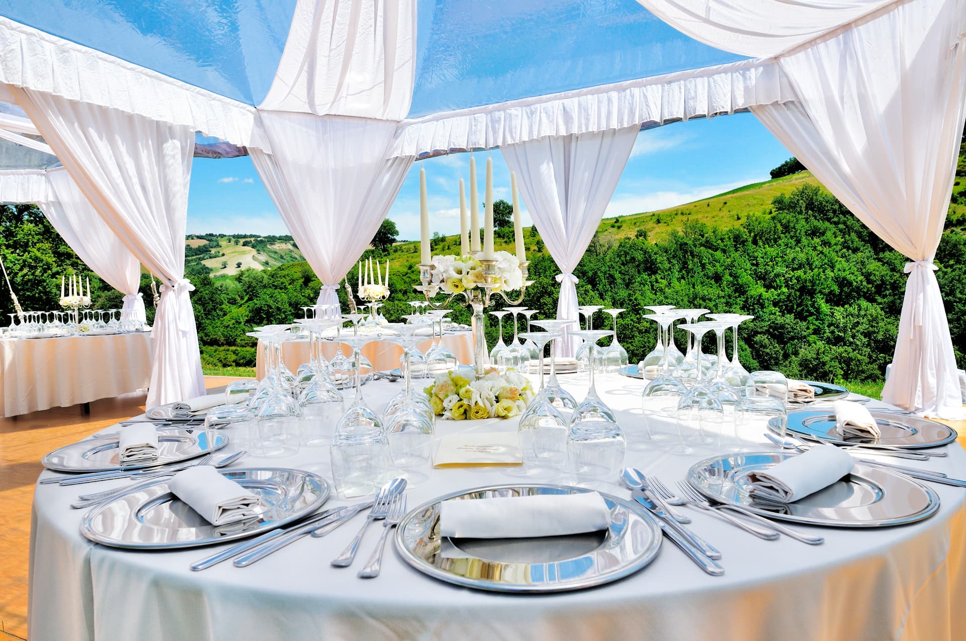 Elegant tented wedding table set with silver chargers, candelabra and white florals