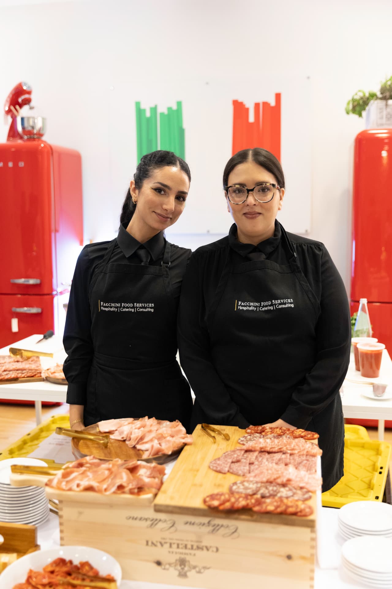 Two Facchini Food Services catering staff behind an Italian charcuterie and antipasti display